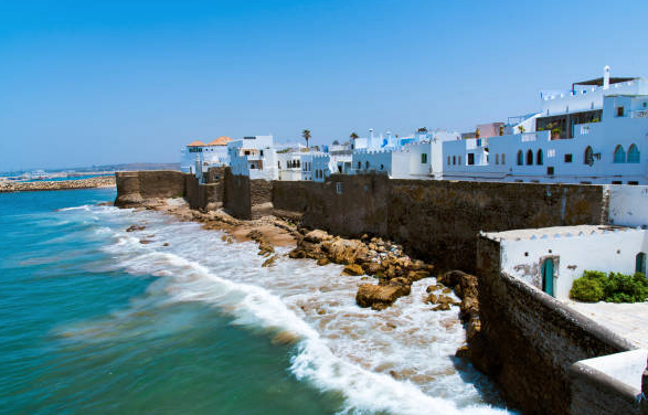 "Una vista panorámica de las murallas medievales de Asilah, rodeadas de casas de colores y una impresionante vista al mar en el fondo. Un lugar perfecto para sumergirse en la historia y la belleza natural de esta ciudad marroquí"



